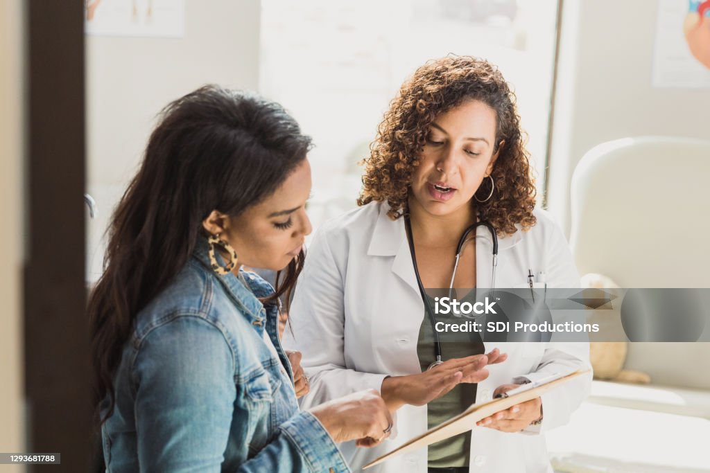 Pediatrician talks with patient's mother A female doctor discusses a young patient's diagnosis with the patient's mother. They are reviewing the patient's test resutls. Doctor Stock Photo