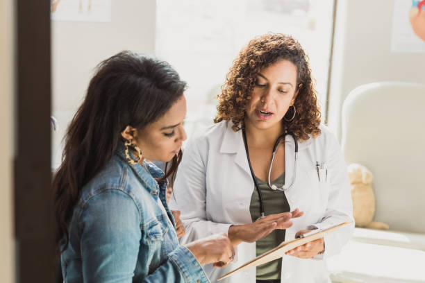 Pediatrician talks with patient's mother A female doctor discusses a young patient's diagnosis with the patient's mother. They are reviewing the patient's test resutls. woman talking to doctor stock pictures, royalty-free photos & images