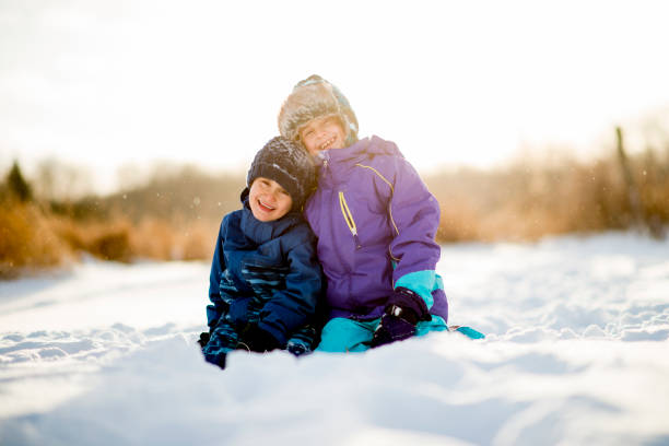 A pair of siblings embracing each other while they are outdoors playing in the snow during the winter.