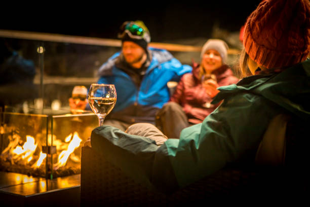 Friends sitting by fire at ski apres at night. Friends enjoying drinks by fire at outdoor patio in a pub apres ski stock pictures, royalty-free photos & images