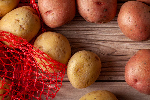 istock Flat lay  close up image featuring a red mesh potato sack with pink and yellow raw organic potatoes on wooden background 1293687249