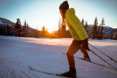 Alone woman cross country skiing at sunset in ski resort.