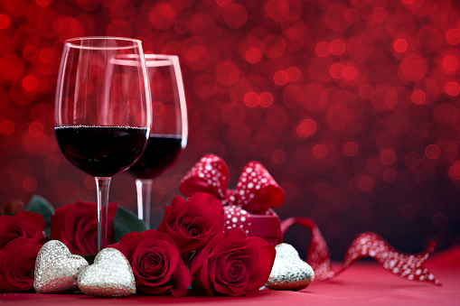 Valentine's Day Red Roses and Red Wine with a Gift on a Defocused Lights Background