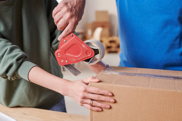 istock Close-up of unrecognizable postal workers packing parcel together using duct tape 1293702772