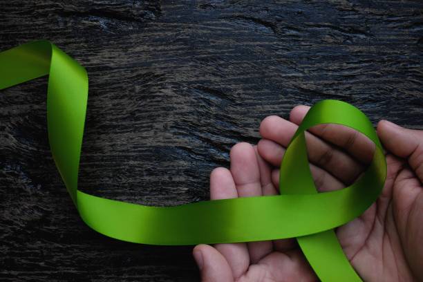 top view of hands holding lime green color ribbon on dark background. non-hodgkin lymphoma cancer, lyme disease, muscular dystrophy and postpartum depression awareness concept - non hodgkin lymphoma imagens e fotografias de stock