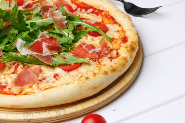 Caesar pizza on board on white wooden table close up