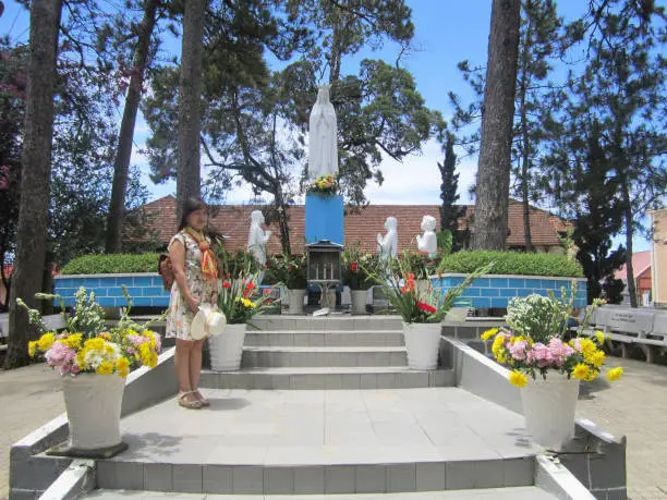 Photo of A woman stands below the statue of the Virgin Mary at Dalat, Viet nam