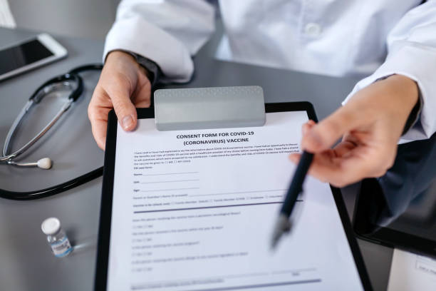 Unrecognizable doctor offering pen to sign coronavirus vaccine consent form Unrecognizable female doctor offering a pen to sign the coronavirus vaccine consent form herd immunity photos stock pictures, royalty-free photos & images
