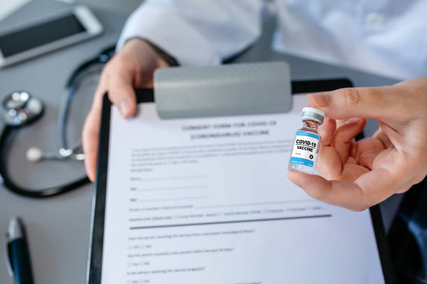 Female doctor's hand showing coronavirus vaccine vial Detail of female doctor's hand showing coronavirus vaccine vial and consent form. Selective focus on vaccine vial in foreground herd immunity photos stock pictures, royalty-free photos & images