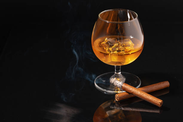 istock Glass of whisky and lighted cigar on black background 1293719014