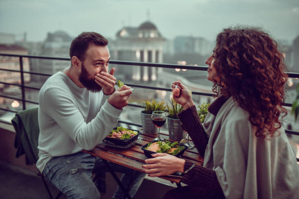 couple smiling and enjoying date with lunch on building rooftop - dating restaurant dinner couple imagens e fotografias de stock