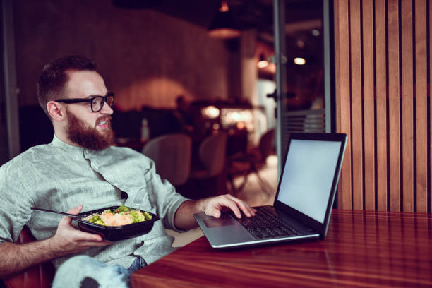 Male Relaxing With His Tuna Salad Lunch And Using Laptop Male Relaxing With His Tuna Salad Lunch And Using Laptop caesar salad food salad tuna stock pictures, royalty-free photos & images