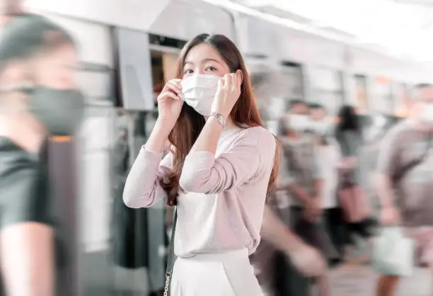 Photo of Asian woman wearing mask and standing amonh people at railway station