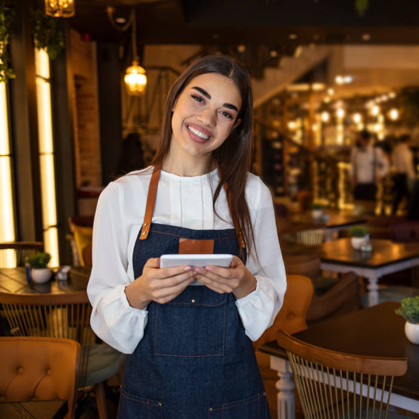 istock Portrait of friendly waitress holding a tablet computer looking at the camera smiling 1293735250