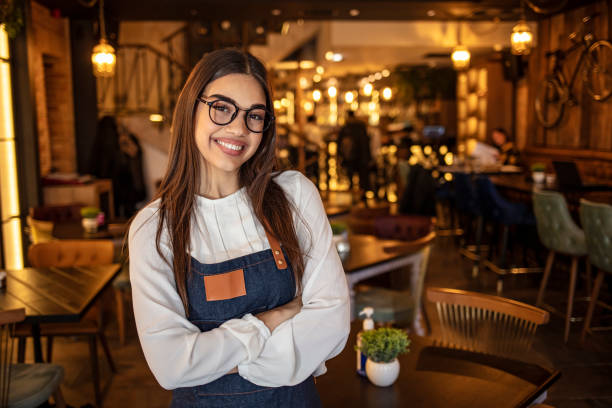 Small business owner at entrance looking at camera Portrait of a confident young woman standing in the doorway of a coffee shop. Portrait of Smiling cafeteria owner. Small business owner at entrance looking at camera television host stock pictures, royalty-free photos & images