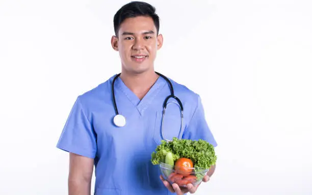 Photo of Asian doctor presenting vegetables and standing on white background