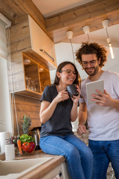 pareja usando tablet y bebiendo café en la cocina - standing digital tablet couple love fotografías e imágenes de stock