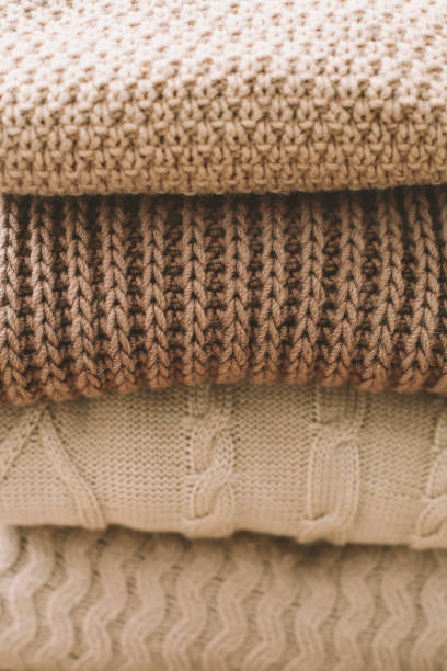 istock Pile of woolen plaids on a light background. Woven fabrics of different patterns arranged in layers. Stack of knitted clothes (sweaters, scarves, pullovers). 1293747777