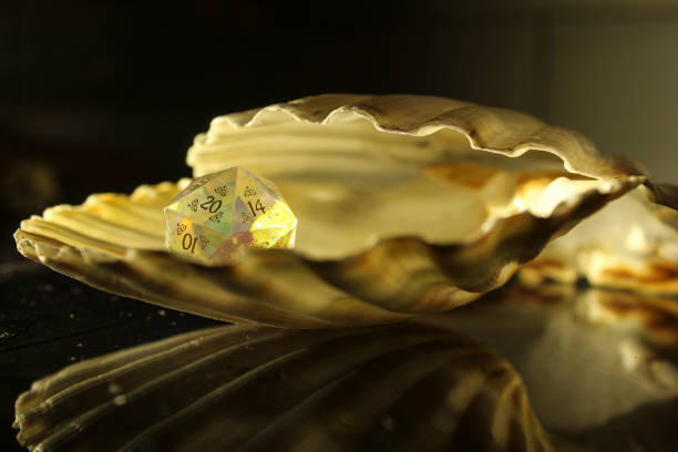 A glass crystal D20 dice from the role-playing game 'Dungeons & Dragons' inside of a bivalve clam shell on a dark reflective surface and dark background.