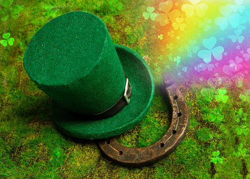 Leprechaun hat and horseshoe lie on green grass with rainbow and clover leaves