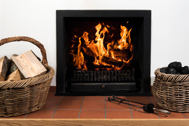Burning fireplace of a fireplace in a living room with a basket of logs on the left and a basket of coal on the right. The fireplace is situated under a mantelpiece in a British home.