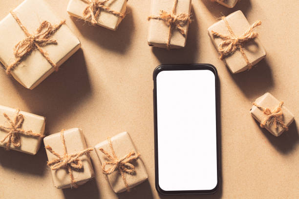 istock Mockup smartphone with blank white screen, new year gift box with Xmas pine tree model, christmas ornaments, santa claus hat on wood background, top view, place for your artwork 1293757522