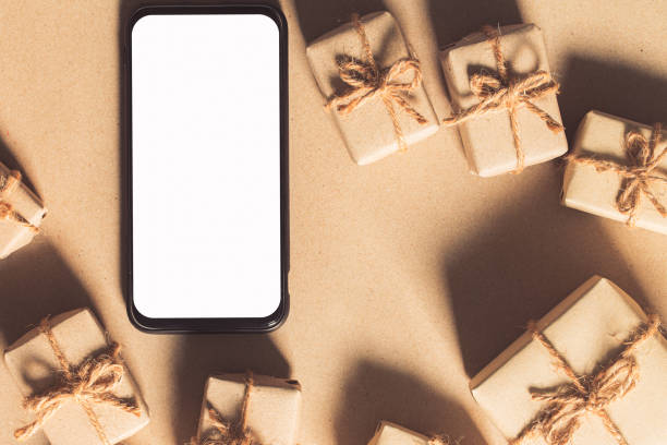 istock Mockup smartphone with blank white screen, new year gift box with Xmas pine tree model, christmas ornaments, santa claus hat on wood background, top view, place for your artwork 1293757541