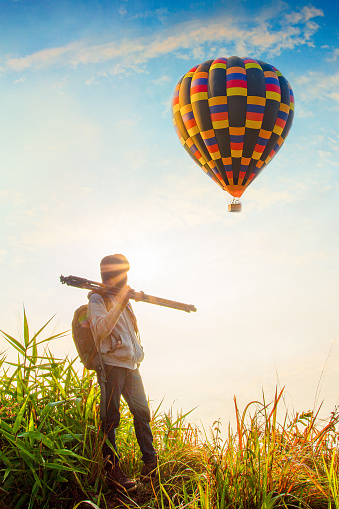 Photographer travels with a camera to capture the sunrise while standing on top of a hill and having a balloon.