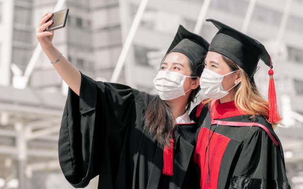 istock Asian female students wearing face mask, graduated uniform and taking selfie 1293763332