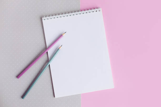 istock Notebook with blank page and two pencils on a pink and grey background. 1293766642