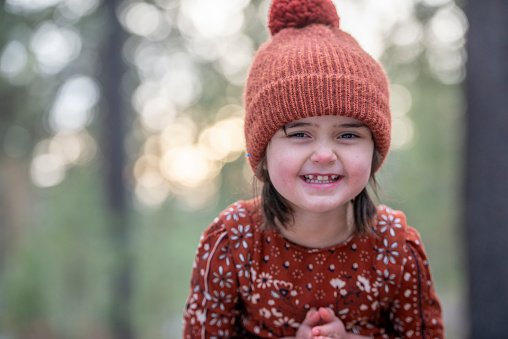 A portrait of a cute little girl smiling for the camera. she wears a knitted hat and a sweater.