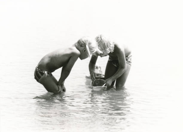 Two young children playing with toy boats in the Mediterranean sea. 1977 vintage, seventies, retro monochrome image of two young children playing with toy boats in the Mediterranean sea in the French coastal village Bretignolles-sur-Mer. french riviera photos stock pictures, royalty-free photos & images