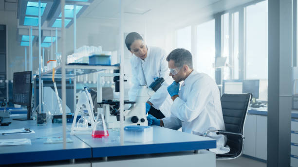 istock Modern Medical Research Laboratory: Portrait of Two Scientists Working, Using Microscope, Analyzing Samples, Talking. Advanced Scientific Pharmaceutical Lab for Medicine, Biotechnology Development 1293772998