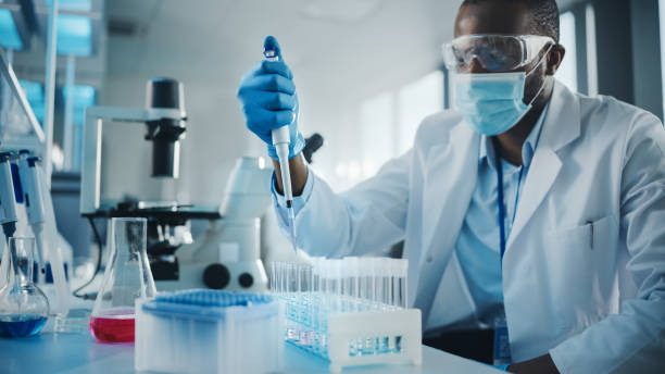 medical development laboratory: black scientist wearing face mask uses pipette for filling test tube with liquid, conducting experiment. pharmaceutical lab with medicine, biotechnology researchers - laboratory doctor white collar worker research imagens e fotografias de stock