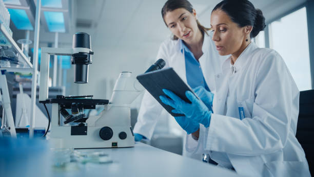 modern medical research laboratory: two female scientists working, using digital tablet, analysing samples, talking. advanced scientific pharmaceutical lab for medicine, biotechnology development - teamwork medical research science women imagens e fotografias de stock