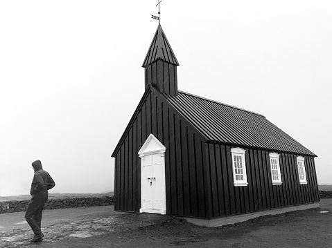 Búðir, Iceland: Man at Black Church (Búðakirkja) in Rain (B&W). Plenty of copy space in the sky.