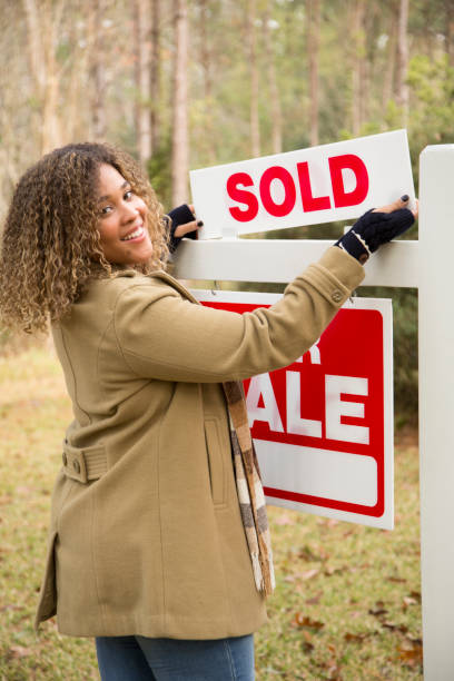 Real Estate Agent.  Home for sale with real estate sign.  Front yard. Home for sale with red and white real estate sign during the fall season.  Fall season with leaves on ground.  Front porch and windows in background.  Residential neighborhood.  Moving house, relocation concept.  Real Estate Agent putting up signs. real estate outdoors vertical usa stock pictures, royalty-free photos & images