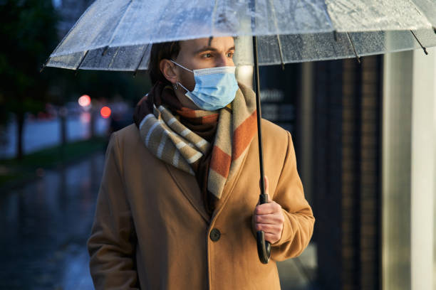 istock Stylish man wearing protective mask with umbrella 1293782141