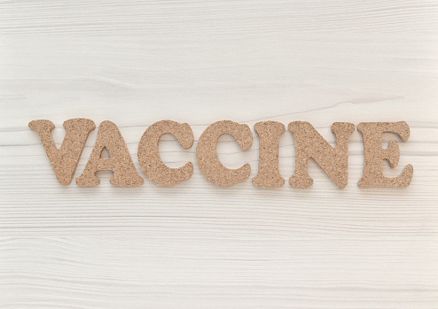 Closeup of the word vaccine spelled out in cork lettering on a whitewashed wood background