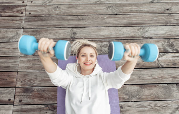 Young fitness woman practicing lying dumbbell press on mat outdoors. Healthy lifestyle Young fitness woman practicing lying dumbbell press on mat outdoors. Healthy lifestyle beach mat stock pictures, royalty-free photos & images