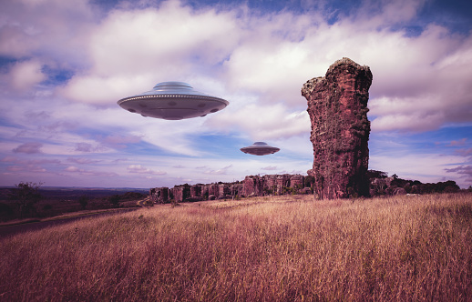 Two UFOs flying over ancient rocks. Unidentified flying objects flying over the sky. 3D illustration with clipping mask included.