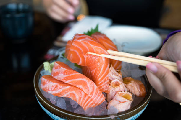 istock Hand with chopsticks holding sashimi sliced salmon on bowl 1293787883