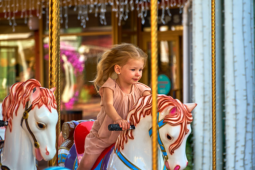 Pretty kid on a carousel horse. A cute girl is riding the attraction. Fun and celebration for children.