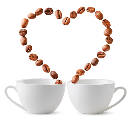 Two cups and coffee beans are flying in the form of a heart on a white background. Isolated