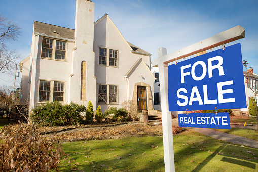 A classic Tudor style house in the mid-west of United States for sale with sale sign on lawn. The two stories property with an old world facade, featuring a fire place chimney.