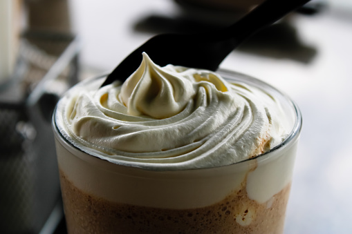 High angle closeup of chocolate milkshake with whipped cream half mixed in and plastic spoon with focus on the foreground