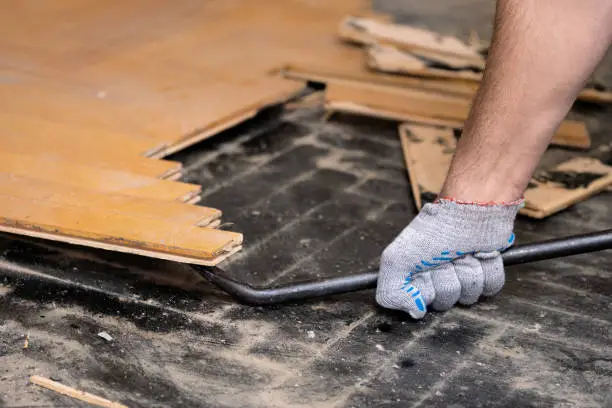 Worker removes old parquet using a tire iron tool during a flat renovation close up