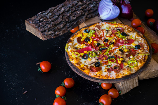 Close-up of mix pizza with mozzarella cheese, sausage and kind of vegetables on black background