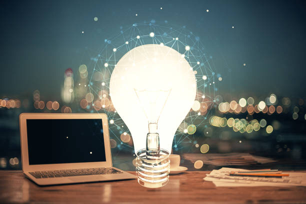 istock Computer on desktop in office with bulb icon hologram. Multi exposure. Concept of idea. 1293807541