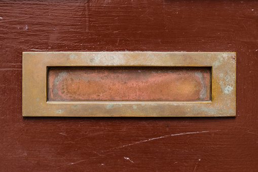 Closeup of an old wooden front door, with brass mail slot.